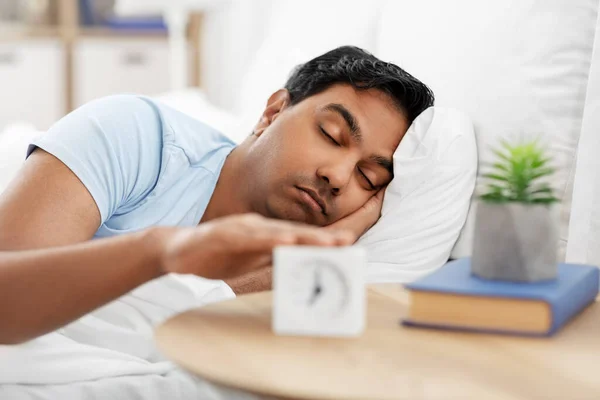 sleepy indian man with alarm clock lying in bed