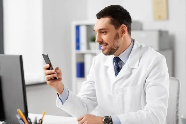 Улыбающийся врач-мужчина со смартфоном в больнице — стоковое фото