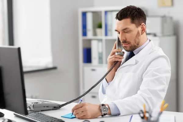 Мужчина врач звонит по настольному телефону в больнице — стоковое фото