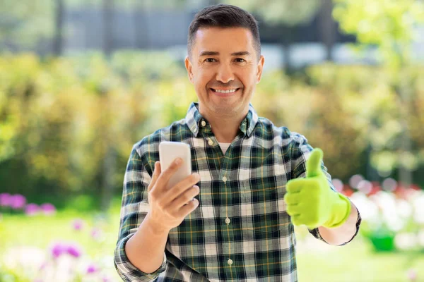 Mężczyzna ze smartfonem pokazuje kciuki w ogrodzie — Zdjęcie stockowe