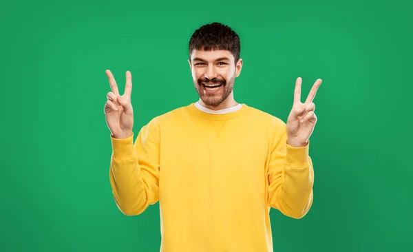 Junger Mann zeigt Frieden vor grauem Hintergrund — Stockfoto