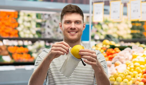 Smiling man putting lemon in reusable grocery tote Stock Image