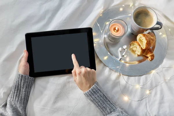 Hands with tablet pc, croissant and coffee in bed — Stock Photo, Image