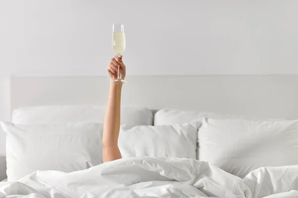 샴페인 잔을 들고 침대에 누워 있는 여자의 손 — 스톡 사진
