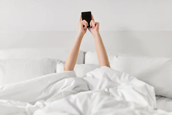 Mãos de mulher deitada na cama com smartphone — Fotografia de Stock