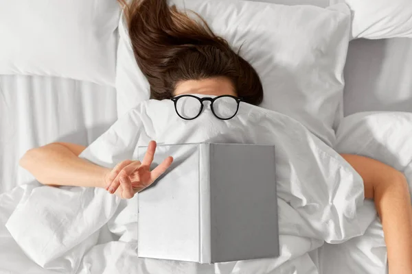 Mujer acostada en la cama con libro y gafas —  Fotos de Stock