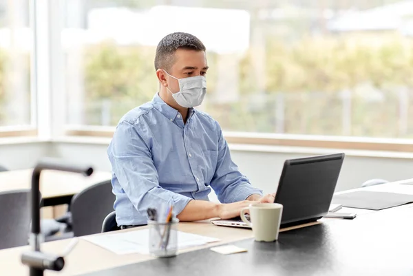 Muž v masce s notebookem pracující v domácí kanceláři — Stock fotografie