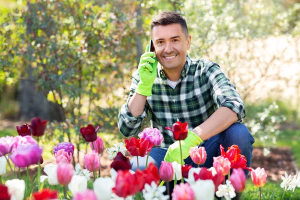 Homem com flores chamando no smartphone no jardim — Fotografia de Stock