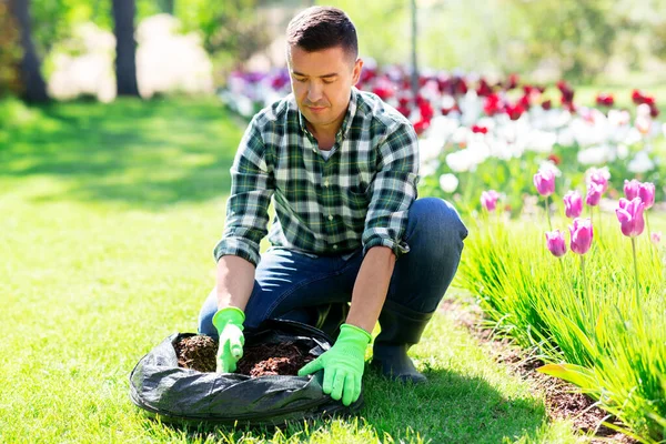 Homme avec de la terre en sac et des fleurs travaillant au jardin — Photo