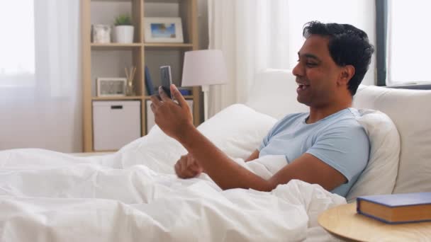 Szczęśliwy Indianin człowiek ze smartfonem w łóżku w domu — Wideo stockowe