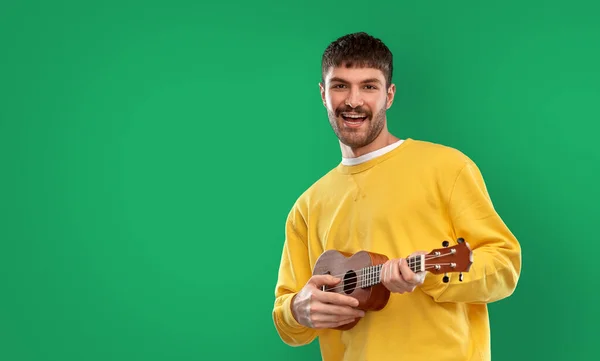 Glücklicher Mann spielt Ukulele-Gitarre über grün — Stockfoto