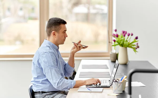 Homem com smartphone e laptop no escritório em casa — Fotografia de Stock