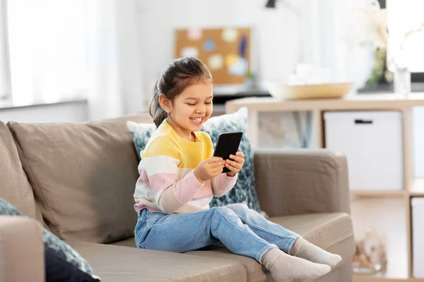 快乐的微笑着的小女孩，家里带着智能手机 — 图库照片