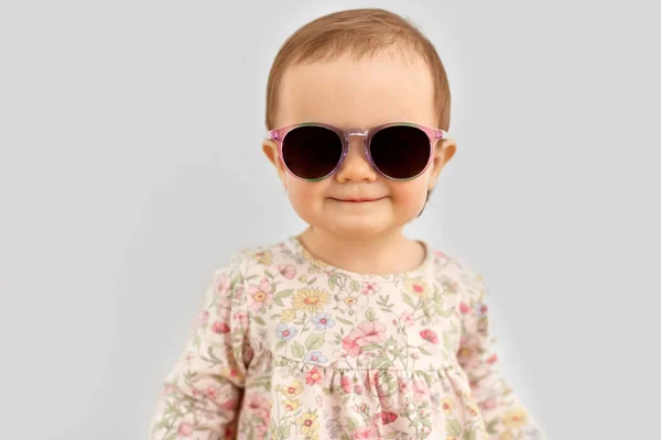 Happy little baby girl in sunglasses over grey — Stock Photo, Image