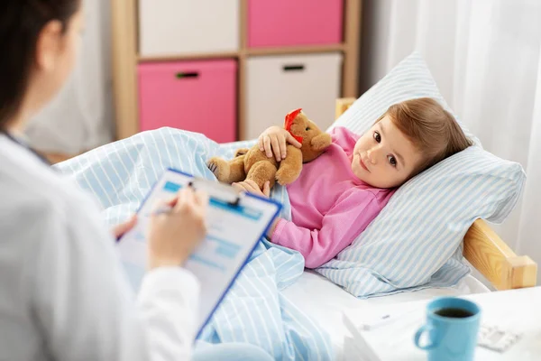 Médico con portapapeles y chica enferma en la cama en casa —  Fotos de Stock