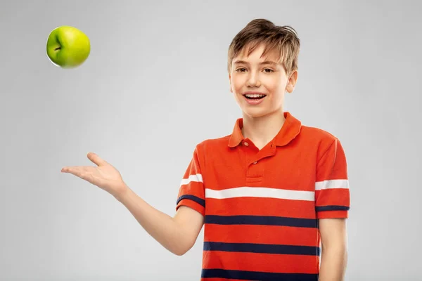 Портрет счастливого улыбающегося мальчика, бросающего зеленое яблоко — стоковое фото