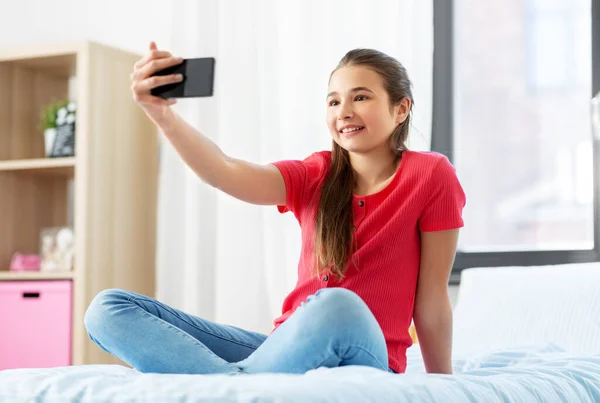 Menina feliz com smartphone levando selfie em casa — Fotografia de Stock