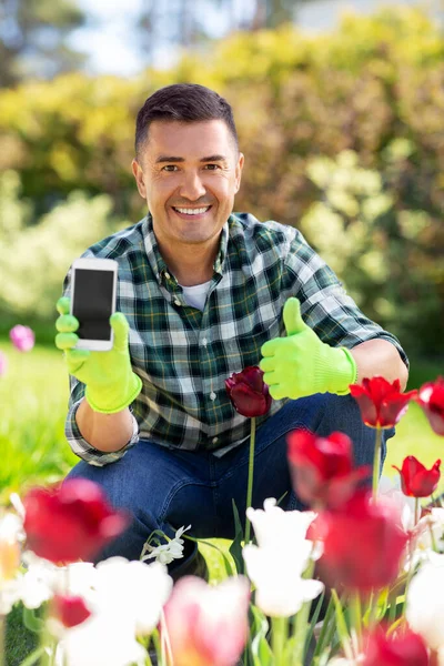 Mężczyzna z telefonem pokazujący kciuki w ogrodzie kwiatów — Zdjęcie stockowe