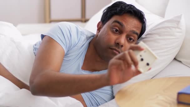 目覚まし時計をベッドに寝そべってインド人男性を目覚めさせ — ストック動画