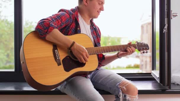 Young man playing guitar sitting on windowsill — Stock Video