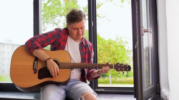 Mladý muž hraje na kytaru sedící na parapetu — Stock video