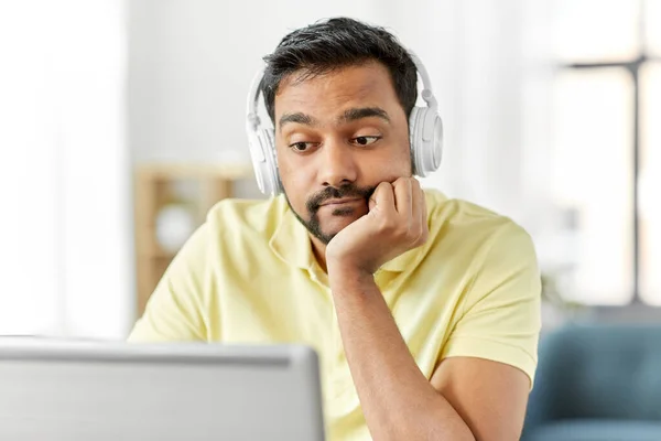 Hombre aburrido en auriculares con portátil funciona en casa —  Fotos de Stock