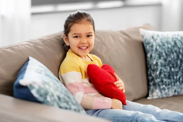 Glad liten flicka med hjärtformad kudde hemma — Stockfoto