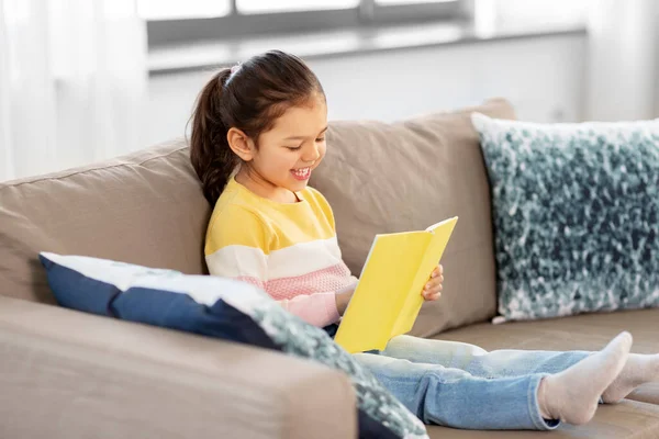 Glad leende liten flicka läsa bok hemma — Stockfoto