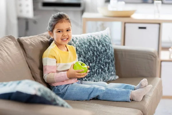 Glad liten flicka med äpple sitter på soffan — Stockfoto