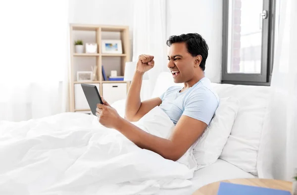 Hombre indio feliz con la tableta PC en la cama en casa —  Fotos de Stock