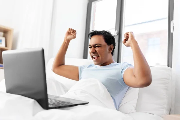 Glad indian man med laptop i sängen hemma — Stockfoto