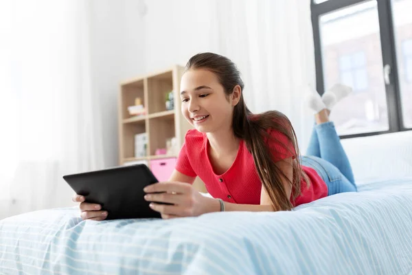 Улыбающаяся девушка с планшетным компьютером, лежащая дома на кровати — стоковое фото