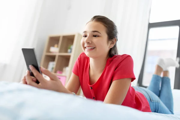 Lächelndes Teenager-Mädchen, das zu Hause auf dem Smartphone SMS schreibt — Stockfoto