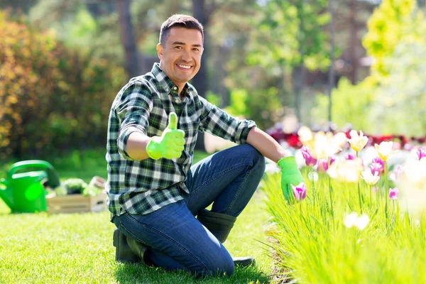 Homme heureux avec des fleurs montrant pouces vers le haut au jardin — Photo