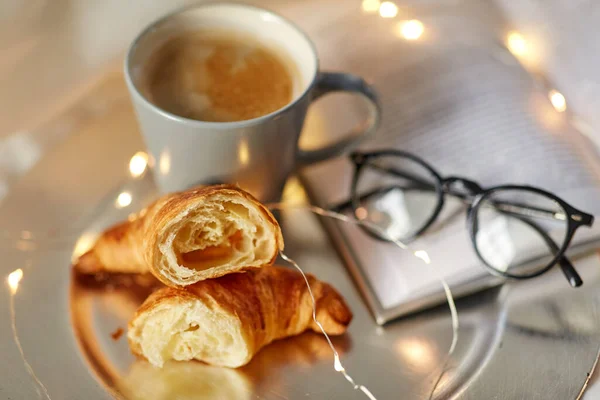 Cornetti, tazzina di caffè, libro e bicchieri a letto — Foto Stock