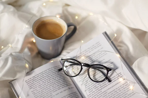 Tasse Kaffee, Buch, Gläser und Girlanden im Bett — Stockfoto