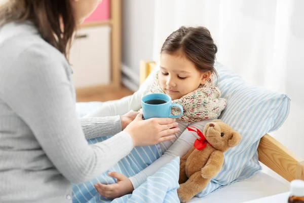 Madre dando té caliente a la pequeña hija enferma — Foto de Stock