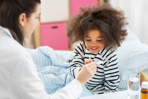 Doctor showing thermometer to smiling sick girl — Stock Photo, Image