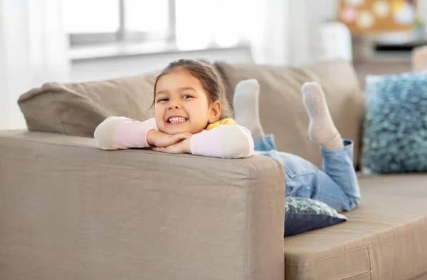 Glad leende liten flicka ligger på soffan hemma — Stockfoto