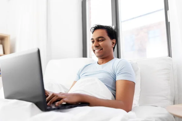 Gelukkig indisch man met laptop in bed thuis — Stockfoto