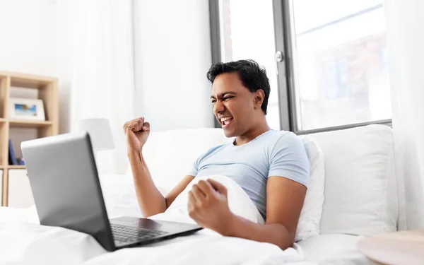 Hombre indio feliz con el ordenador portátil en la cama en casa —  Fotos de Stock