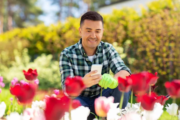 Мужчина среднего возраста со смартфоном в цветочном саду — стоковое фото