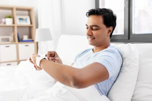 Hombre indio feliz con reloj inteligente en la cama en casa Fotos De Stock Sin Royalties Gratis