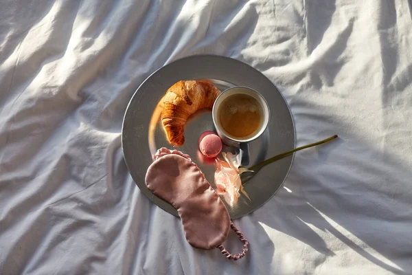 Croissant, kávé és szem alvás maszk az ágyban — Stock Fotó