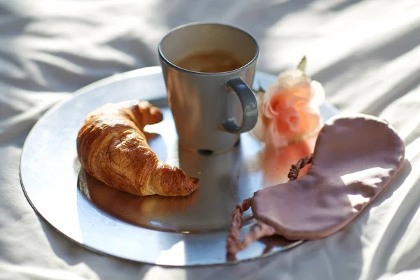 Croissant, koffie en oog slaapmasker in bed — Stockfoto