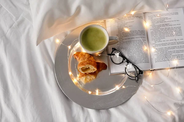 Croissanter, tändstickste, bok och glas i sängen — Stockfoto