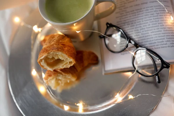 Croissants, chá matcha, livro e óculos na cama — Fotografia de Stock