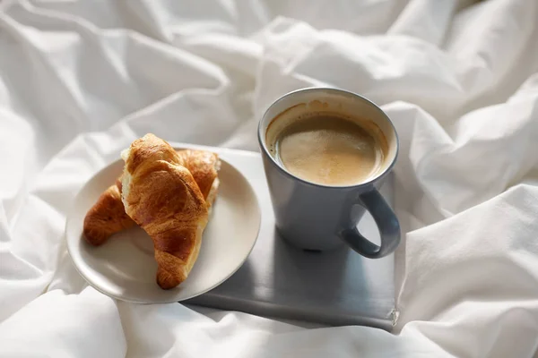 Croissants, cup of coffee and book in bed at home — Stock Photo, Image