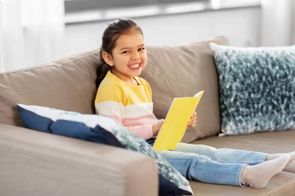 Счастливая улыбающаяся маленькая девочка читает книгу дома — стоковое фото