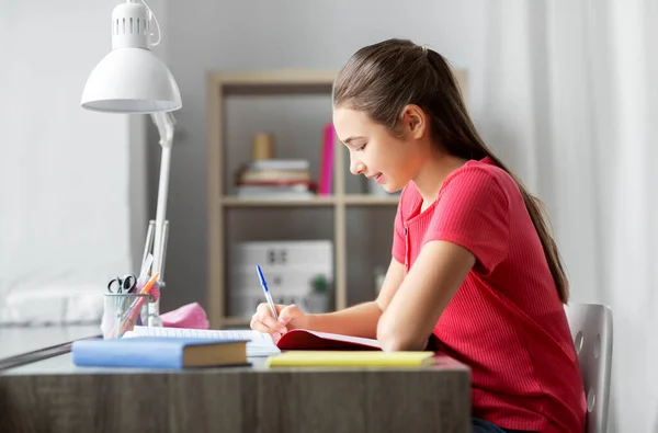 Student girl with book writing to notebook at home — Stock Photo, Image